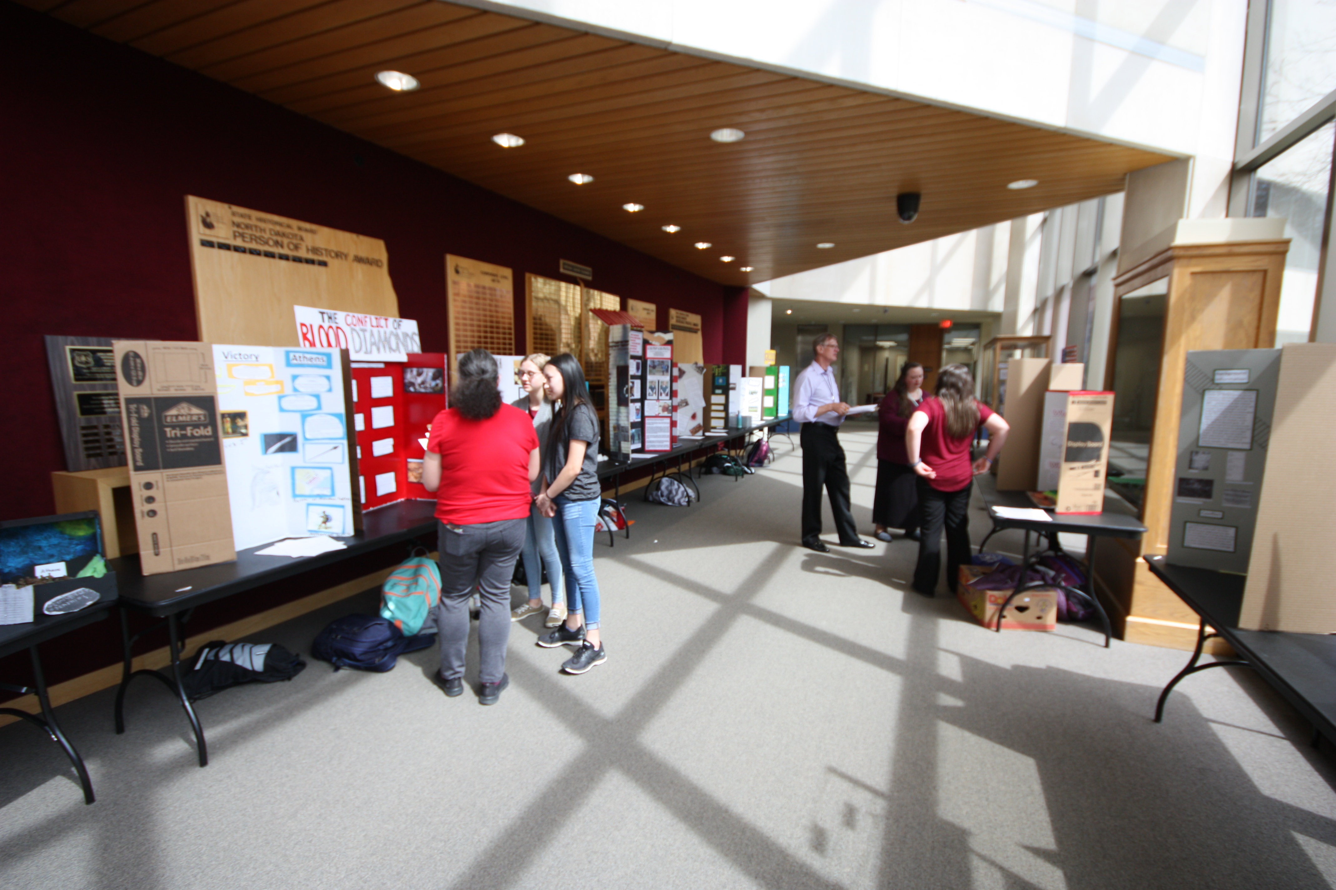 ND Heritage Center with History Day contestant exhibits and judges. Judges inquire about the student's project and score according to the contest guidelines.